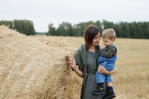 A Woman Carrying a Child While Standing Near the Hay Bale 
