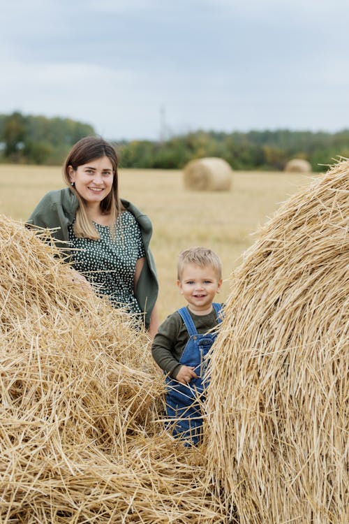 Smiling Woman and Little Boy Standing by Bales on Field