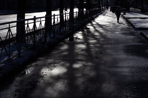 Free A dramatic black and white photo of an urban street with shadows, railing, and walking figure. Stock Photo