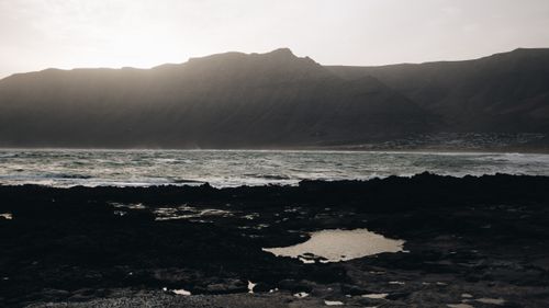 Free A stunning seascape with waves crashing against dark rocks beneath towering mountains. Stock Photo