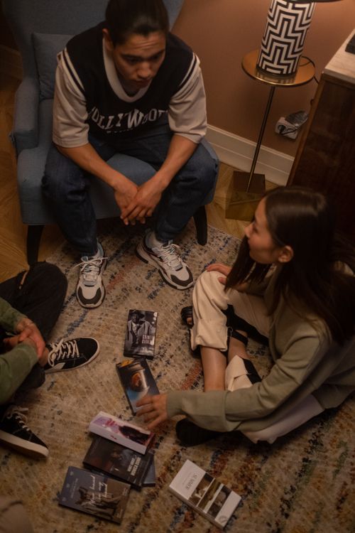 Free Three teenagers sit on a rug discussing movie selections in a cozy indoor setting. Stock Photo