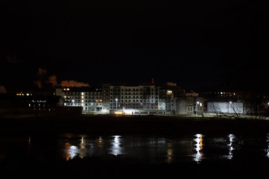 Nighttime cityscape with illuminated buildings reflecting on a river.