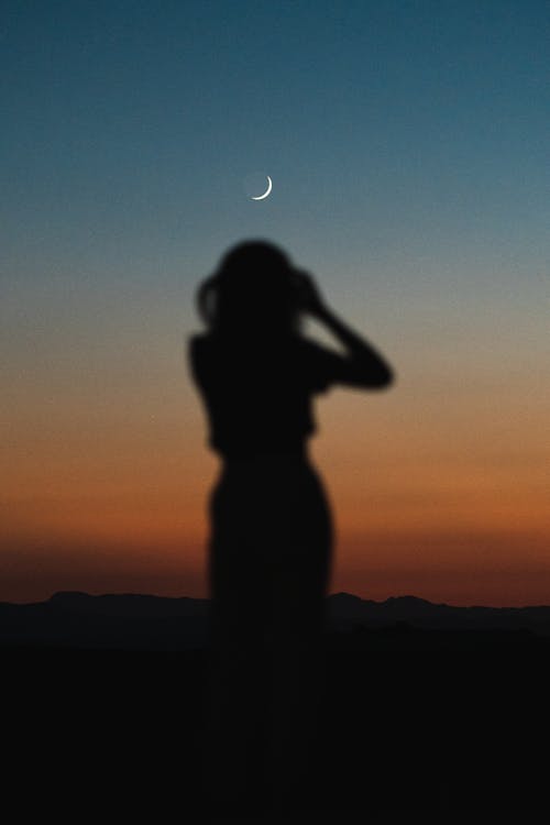 Dark silhouette of person below crescent moon