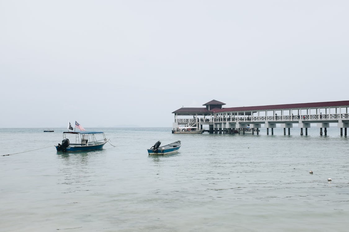 White and Blue Boat on Body of Water Near Pier