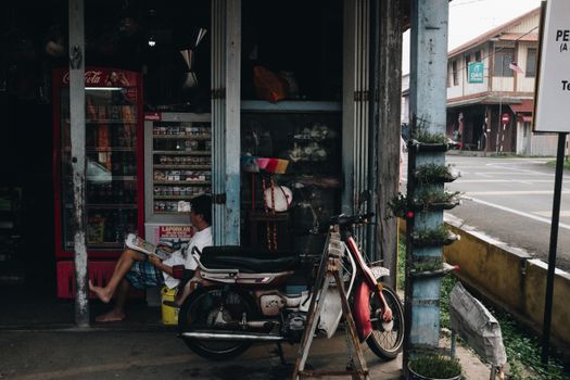 在马来西亚贝苏特，一名男子坐在一家店面旁，骑着摩托车，反映了当地的城市生活