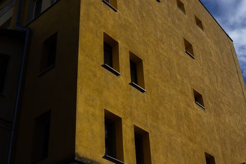 Free A sunlit yellow facade with geometric window patterns creating shadow play. Stock Photo