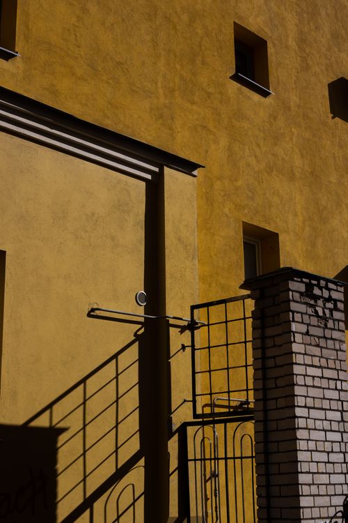 Free Yellow building wall casting shadows from a gate and railing, creating a modern urban scene. Stock Photo