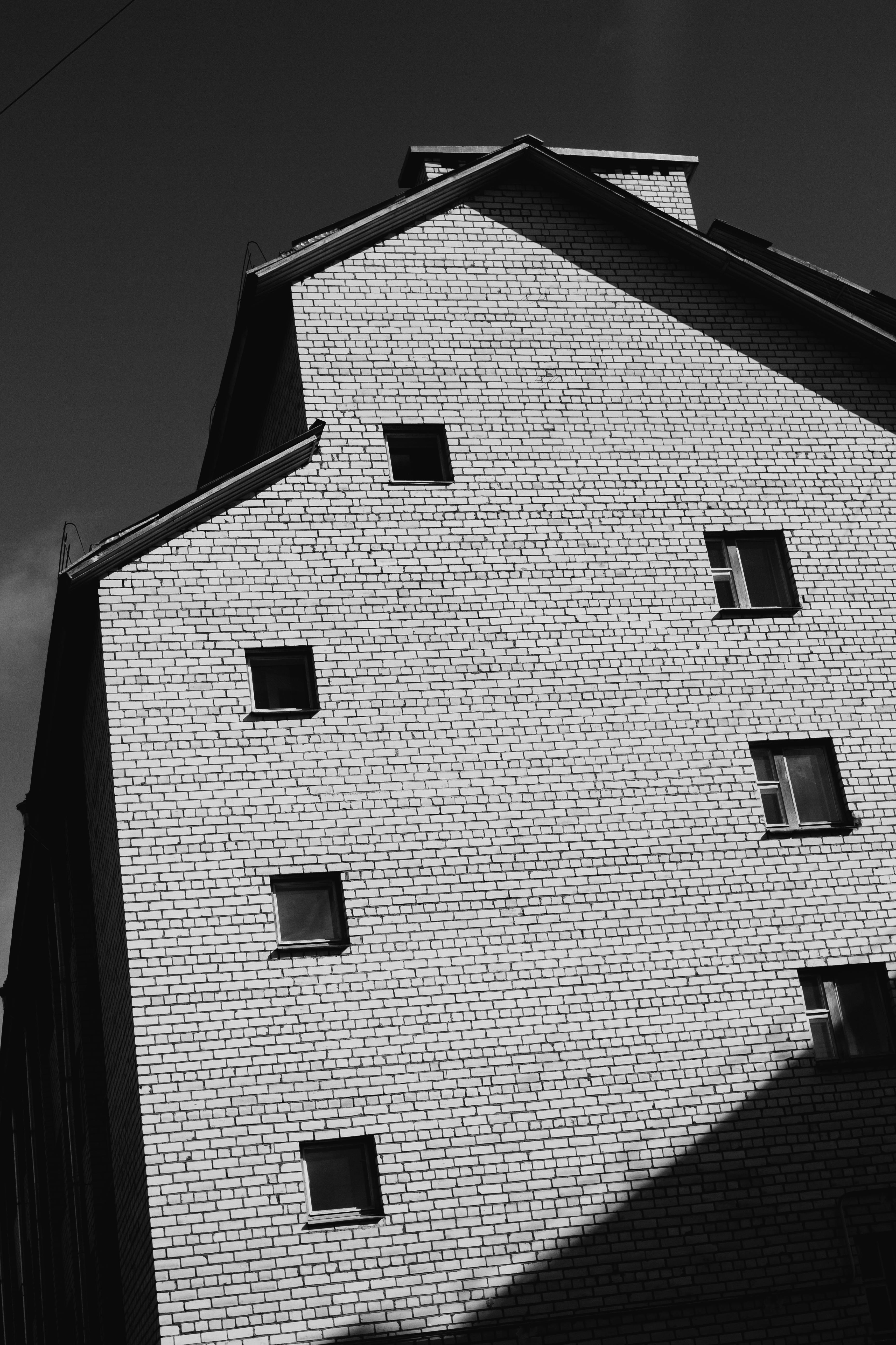 A black and white photo of a brick building exterior with distinct shadows.