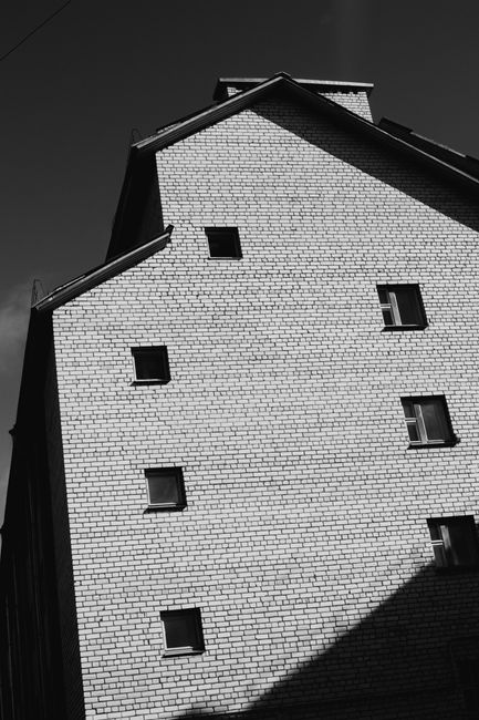 A black and white photo of a brick building exterior with distinct shadows.