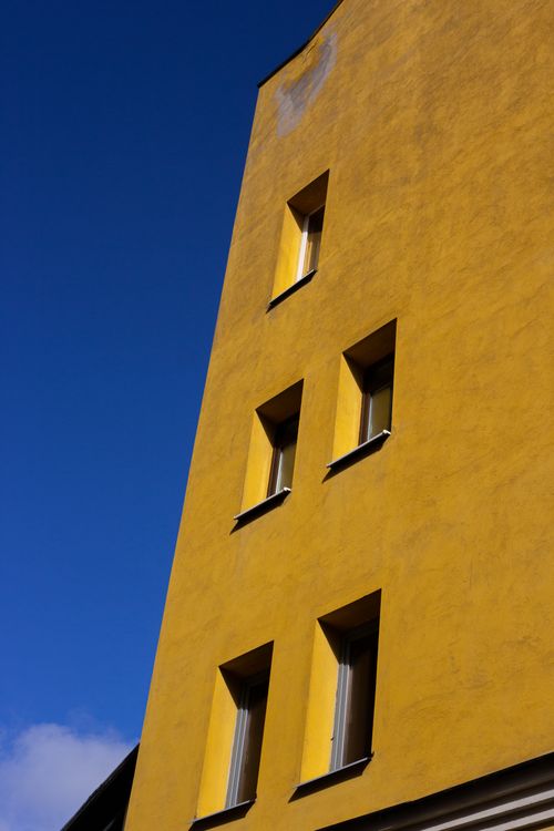Free A striking yellow building facade with multiple windows set against a deep blue sky. Stock Photo