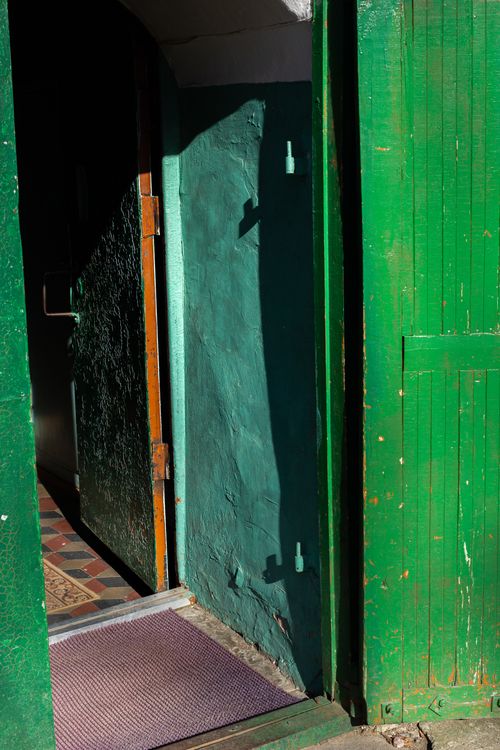 Free Green wooden door slightly ajar with sunlight casting shadows on entrance. Stock Photo