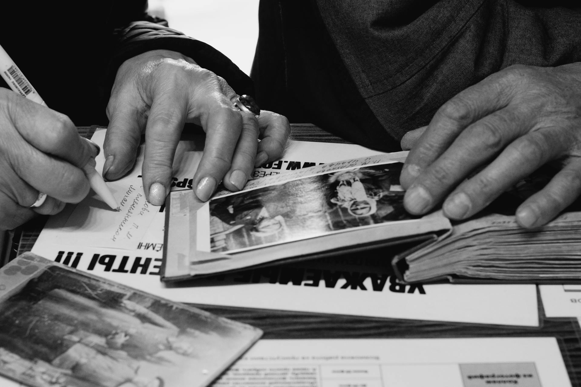 Hands of elderly people examining and writing in photo albums, capturing memories.