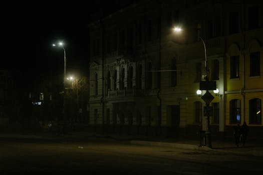 A dimly lit city street at night with vintage architecture and street lamps casting a haunting glow.