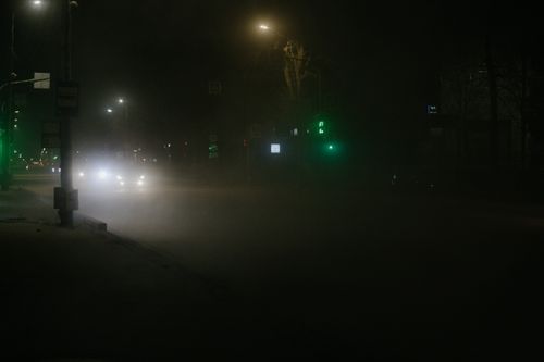 Free A dimly lit urban street at night with fog and glowing traffic signals. Stock Photo