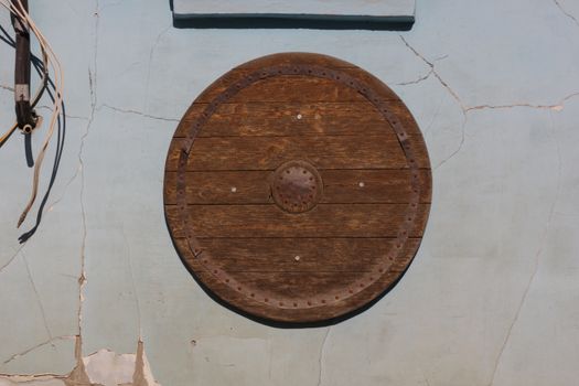 A rustic wooden shield mounted on a weathered, cracked wall with visible cables.
