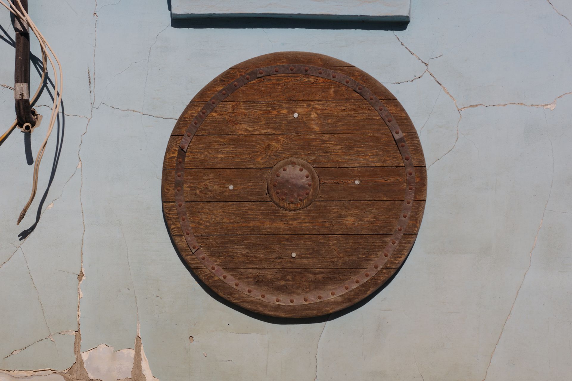 A rustic wooden shield mounted on a weathered, cracked wall with visible cables.