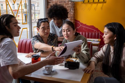 Free A multicultural group of young adults engaged in conversation around a table in a cafe, focused on a document. Stock Photo