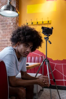 Man seated in vibrant café setting with camcorder on tripod, exuding a cool and modern vibe.
