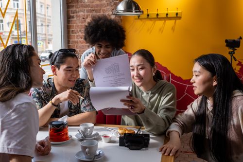 Free A diverse group of young adults enjoys reading a document in a cozy cafe setting. Stock Photo