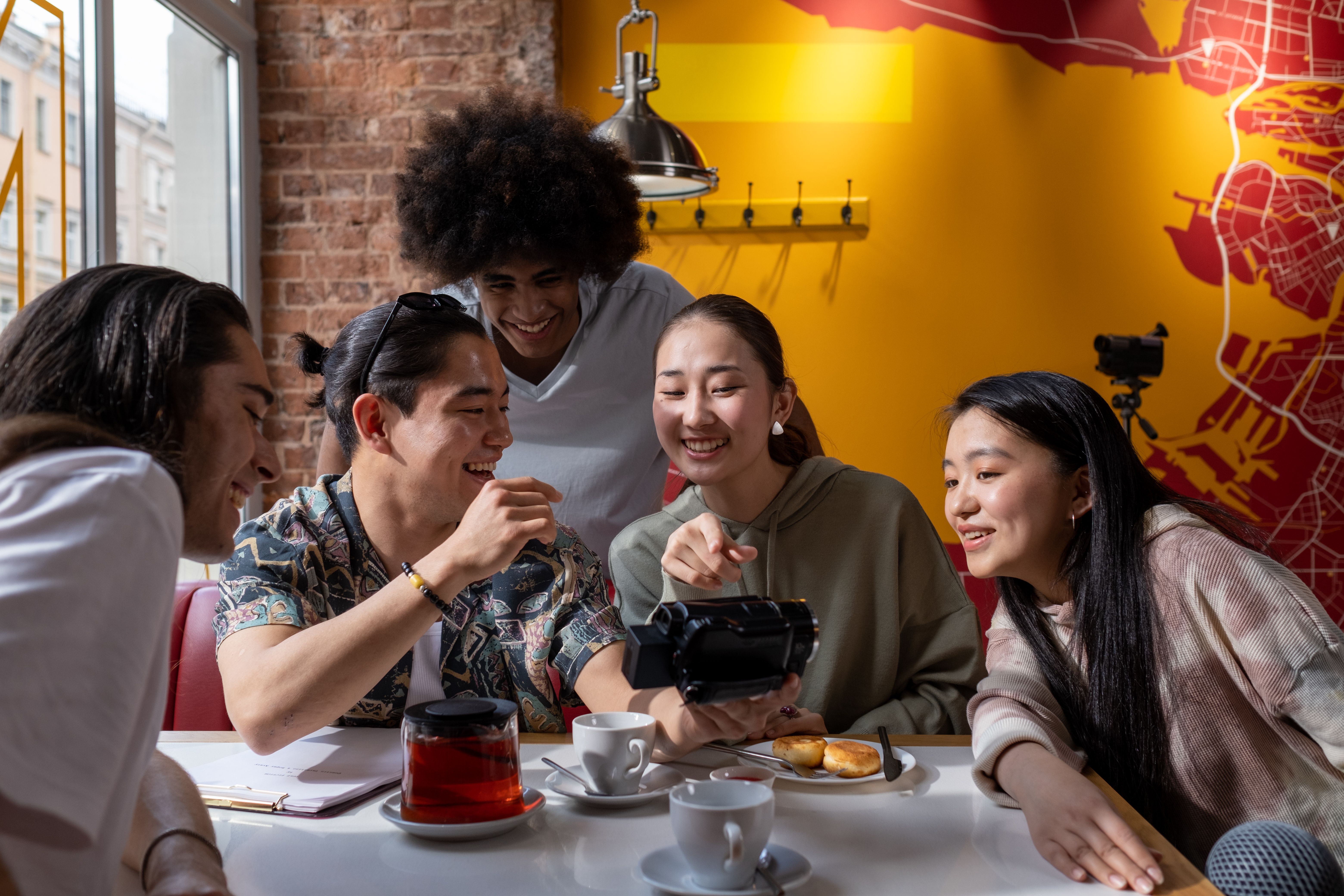 Five friends sharing a fun moment with a camcorder in a cozy cafe.