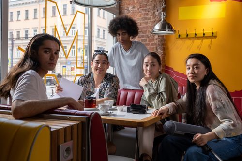 Free Friends relax in a vibrant cafe, sharing smiles and enjoying their time together, surrounded by a colorful and warm atmosphere. Stock Photo