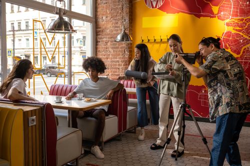 Free A diverse group engages in a casual photoshoot at a vibrant urban café with brick walls and map decor. Stock Photo