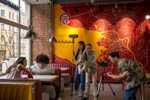 A diverse film crew operates in a trendy urban restaurant with a vibrant map mural.