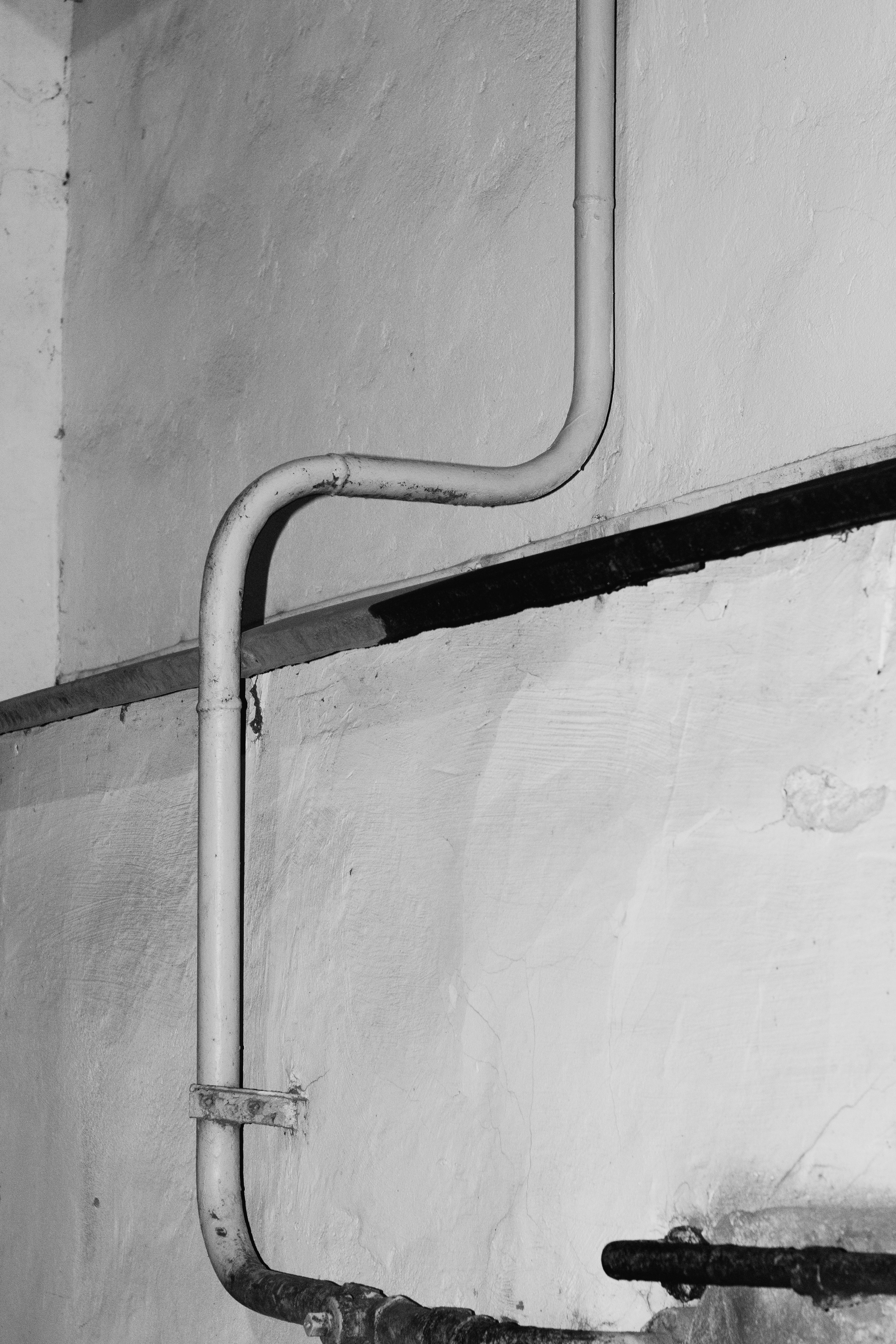 Black and white vertical image of a pipe against a textured concrete wall.