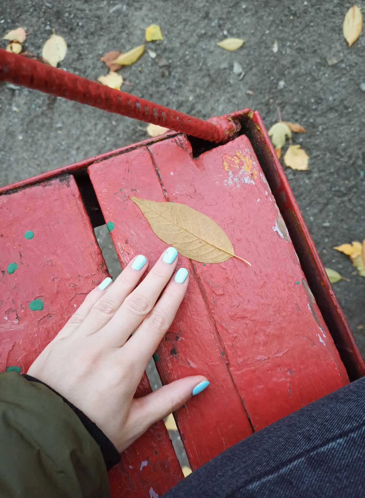 A close-up of a hand with manicured nails touching a leaf on a red wooden swing during fall.