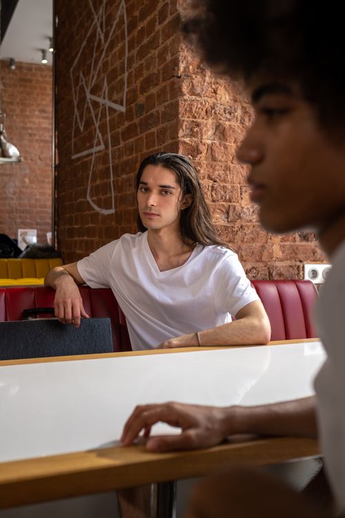 Free Two men in casual clothing sit in a cozy café with exposed brick walls. Stock Photo