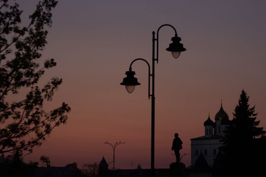 Silhouette of street lamps and church at sunset with clear sky and distant trees.