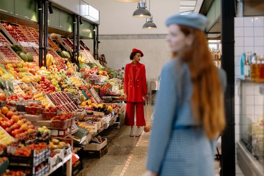 Two stylish women exploring a vibrant fresh produce market indoors.