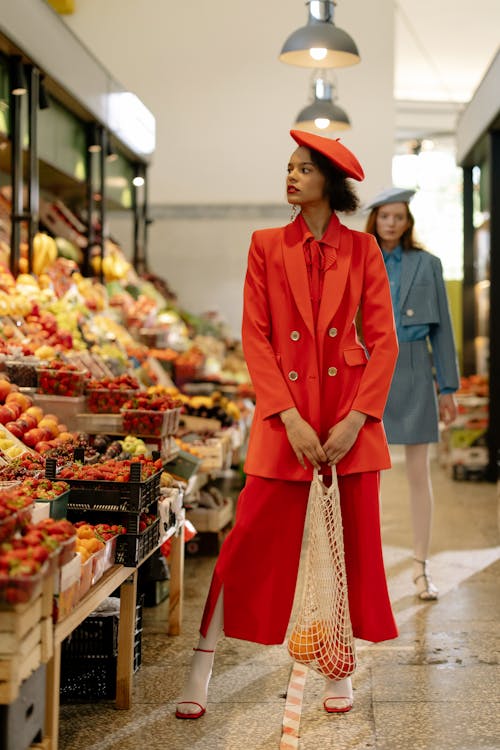 A Woman Standing Near the Fruit Stand while Holding a Mesh Bag