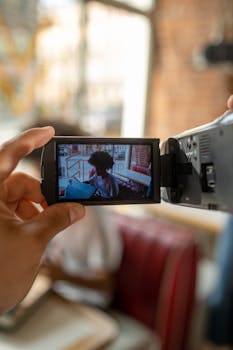 Close-up of hands holding a camcorder recording a scene inside a cafe.