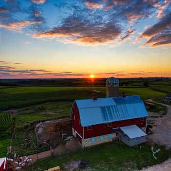 Stunning aerial view of a red barn at sunset surrounded by lush fields in Minnesota's countryside.