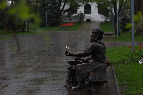 Statue of a Man Sitting on Wooden Bench in the Park