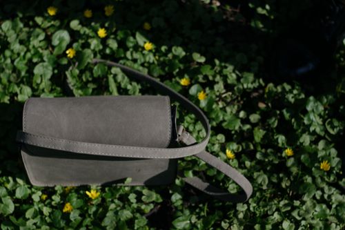 Free A stylish green handbag resting on lush foliage with yellow wildflowers, perfect for spring fashion themes. Stock Photo