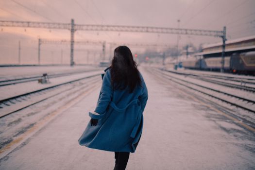 A woman in a blue coat walks on a snowy railway platform during winter.