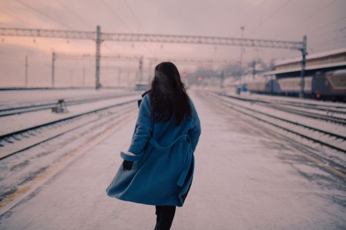 Free A woman in a blue coat walks on a snowy railway platform during winter. Stock Photo