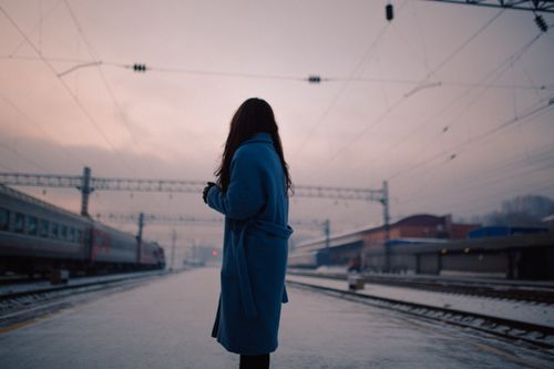 Free A woman in a blue coat stands at a train station during the evening. Stock Photo