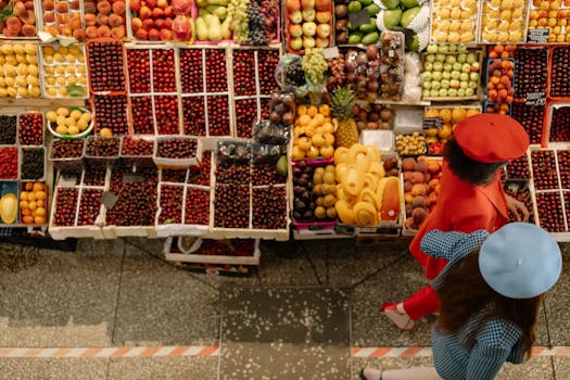 Overhead view of vibrant fruit market stand with two stylish shoppers in berets, showcasing fresh produce.