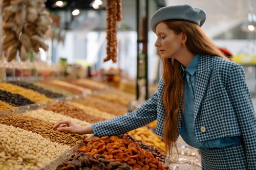 Free Woman in stylish outfit selecting dried fruits and nuts at a market display. Stock Photo