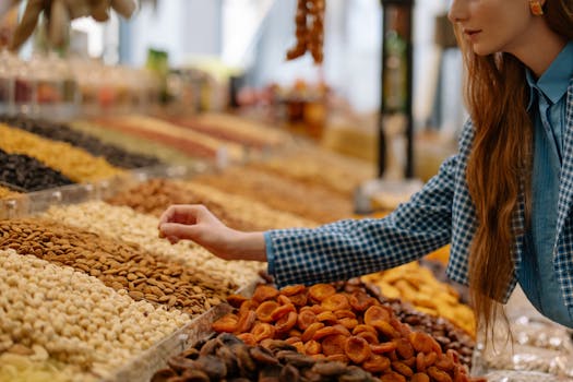 A woman is choosing a variety of nuts at an outdoor market stall, showcasing vibrant colors and textures.