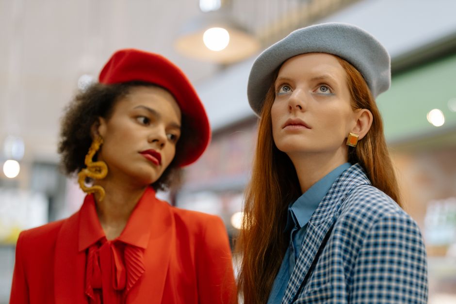 Two fashionable women wearing berets and trendy outfits indoors, embodying modern style.