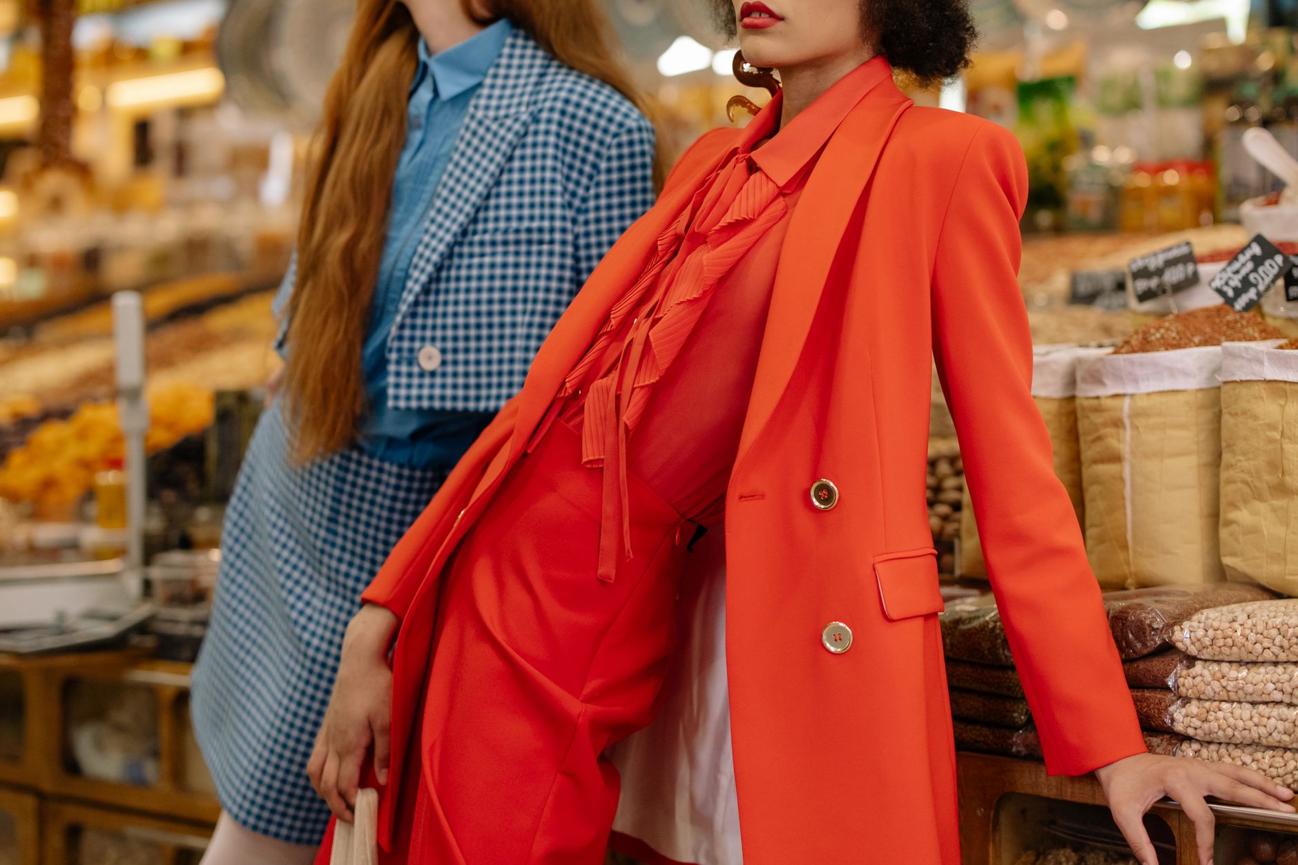 Stylish women in colorful outfits posing at a lively grocery market.