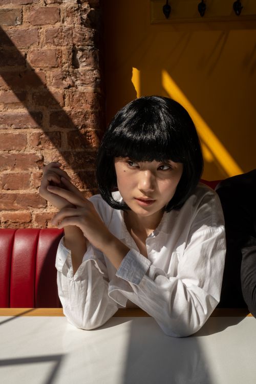 Free A thoughtful woman sits in a brightly lit café, casting a dramatic shadow. Stock Photo