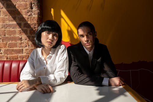 A couple in a stylish setting with contemporary fashion, seated indoors with contrasting lighting.