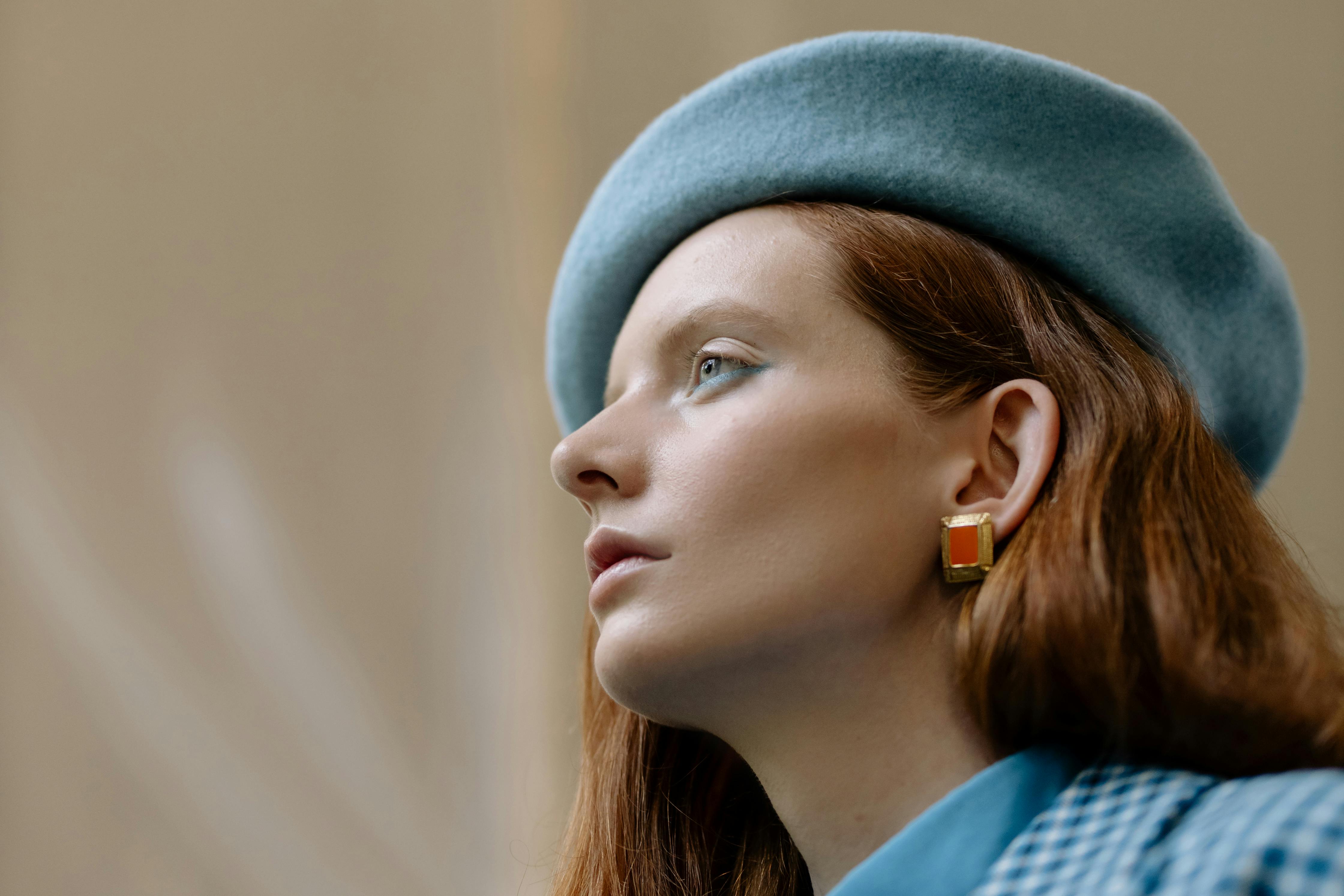 Side portrait of a woman in a blue beret and earrings, showcasing elegance and style.
