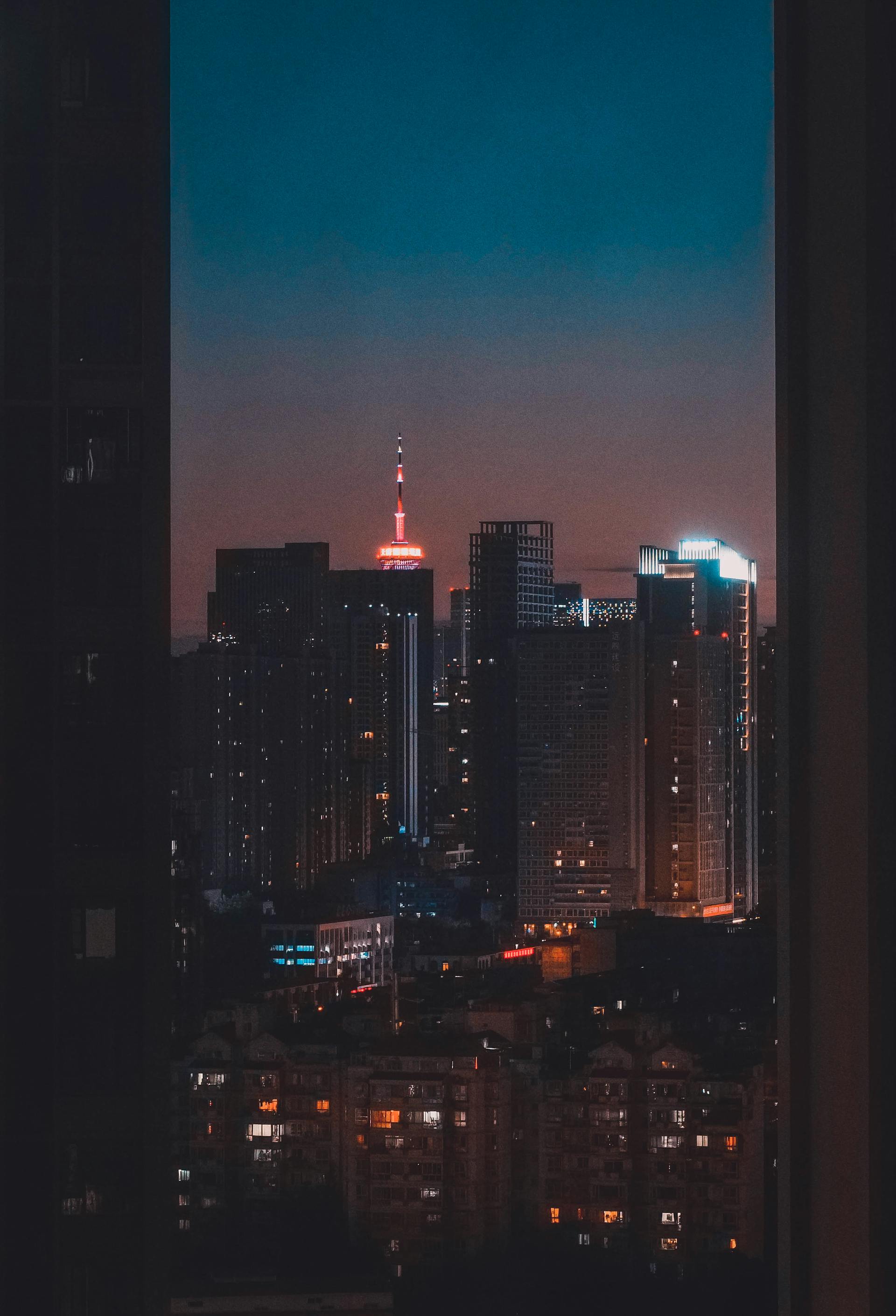 A window view of high-rise buildings at night with city lights