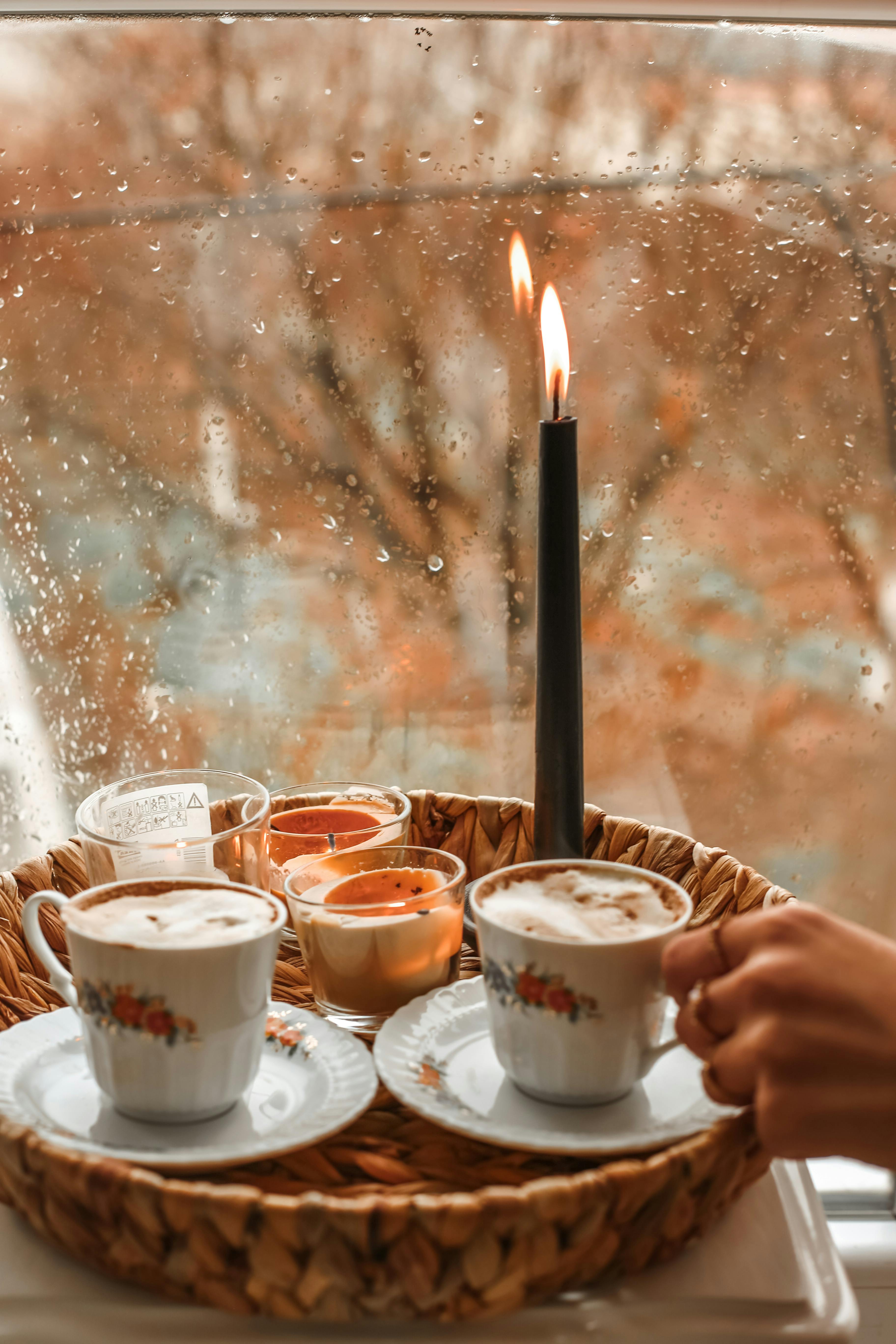 Free Warm indoor scene with coffee and candles by a rainy window, perfect for cozy relaxation. Stock Photo